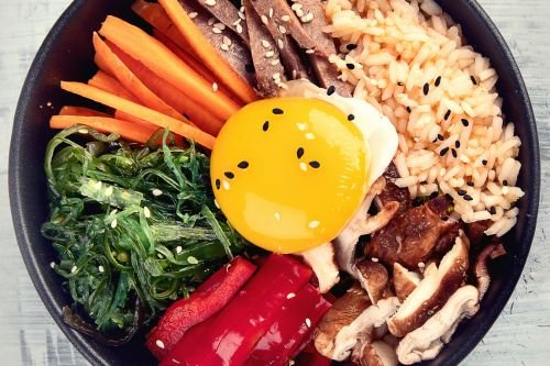 korean bibimbap bowl showing colorful vegetables, rice, and egg on top