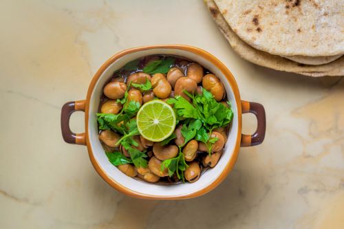 bowl of ful medames showing fava beans topped with olive oil and parsley