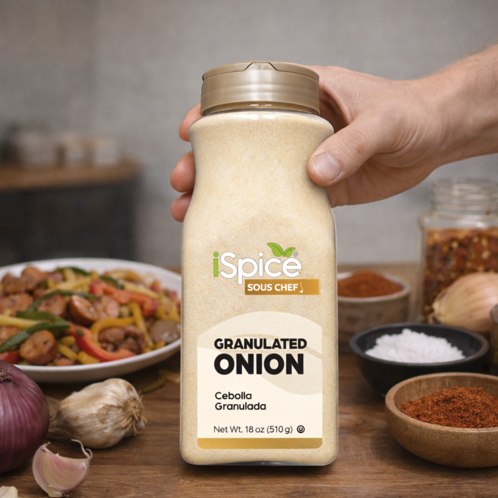 Hand holding a bottle of iSpice Granulated Onion with a background of spices and food.