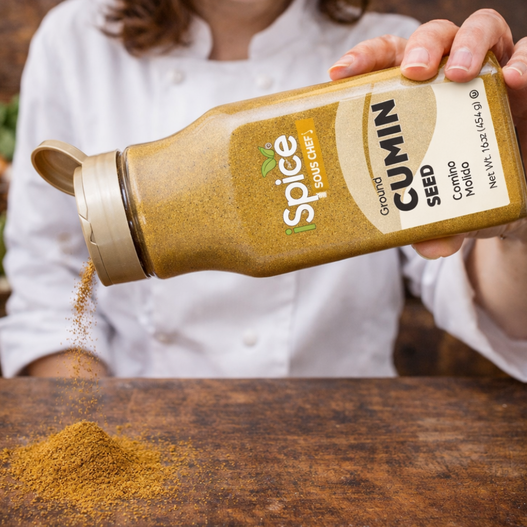 Person pouring cumin spice from a Spice Sou Chef bottle onto a wooden surface.